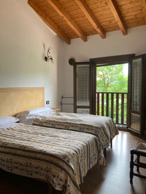 Dormitorio rústico en Casa Lafuente con vigas de madera vista, dos camas y balcón con vistas a montañas verdes en Araba, España