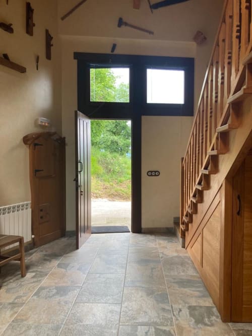 Entrada moderna de apartamento Casa Lafuente con piso de pizarra, elementos de madera y puerta de vidrio con vistas a montaña verde