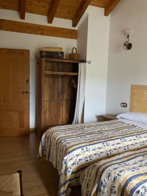 Dormitorio rústico en Casa Lafuente con vigas de madera, colcha estampada, armario antiguo y techo expuesto en Lukiano