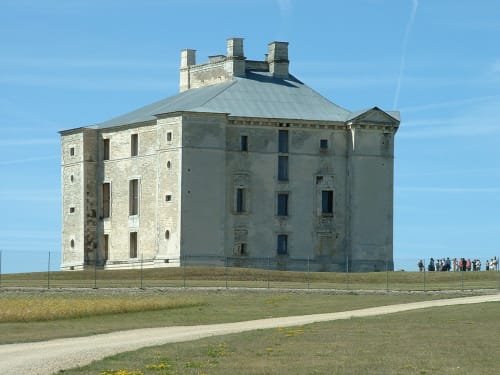 Historic stone tower at Domaine de l'Ocrerie in Pourrain, France with metal fence and visitors on grounds
