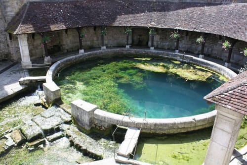 Historic thermal pool at Domaine de l'Ocrerie in Pourrain, France, featuring turquoise water surrounded by stone architecture