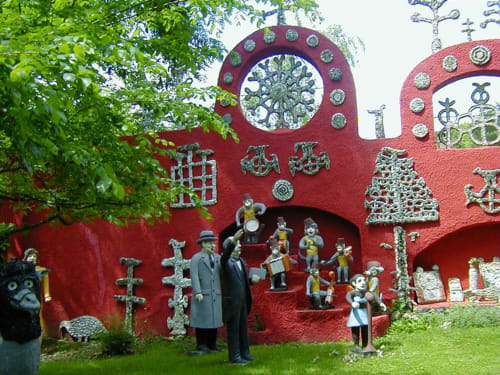 Large red sculptural installation with whimsical characters and architectural details at Domaine de l'Ocrerie in Pourrain