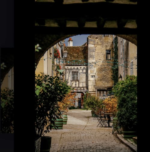 Charming courtyard at Domaine de l'Ocrerie in Pourrain with arched passage, potted plants, and historic stone buildings