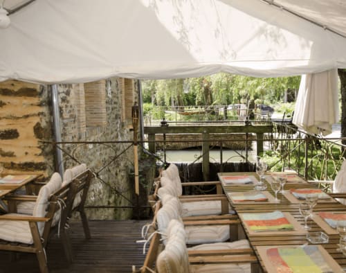 Elegant outdoor dining area at Domaine de l'Ocrerie with set tables, white linens, and canal view under awning