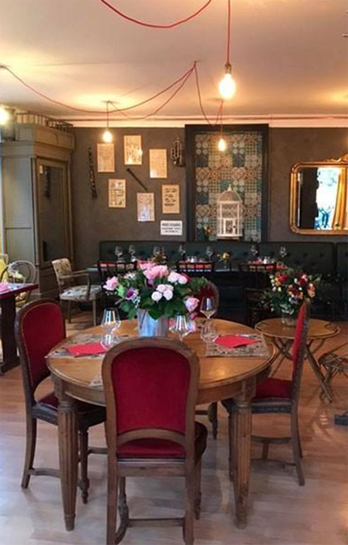 Elegant dining room at Domaine de l'Ocrerie with round wooden tables, red velvet chairs, fresh flowers, and warm lighting in