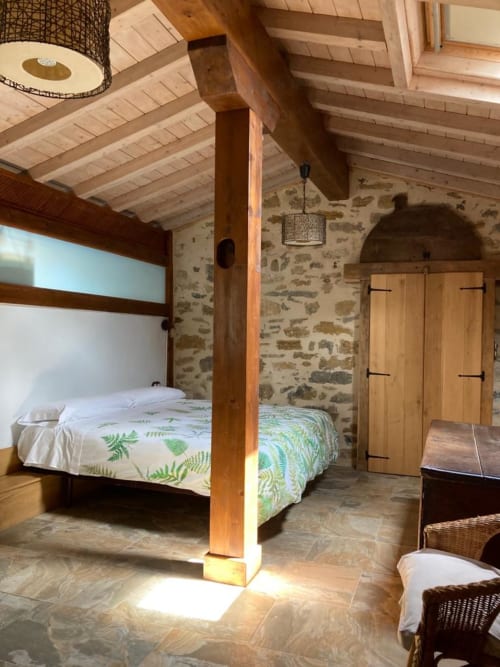 Dormitorio rústico de piedra en Casa Lafuente con vigas de madera, ropa de cama con helechos, vigas expuestas y vistas a la montaña en Lukiano