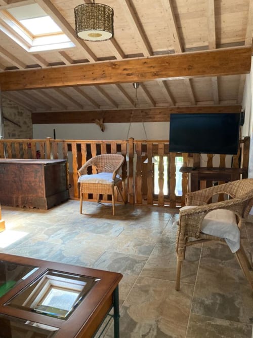 Amplio salón de apartamento en Casa Lafuente con vigas aparentes, mobiliario de ratán, TV de pantalla plana y vistas a las montañas