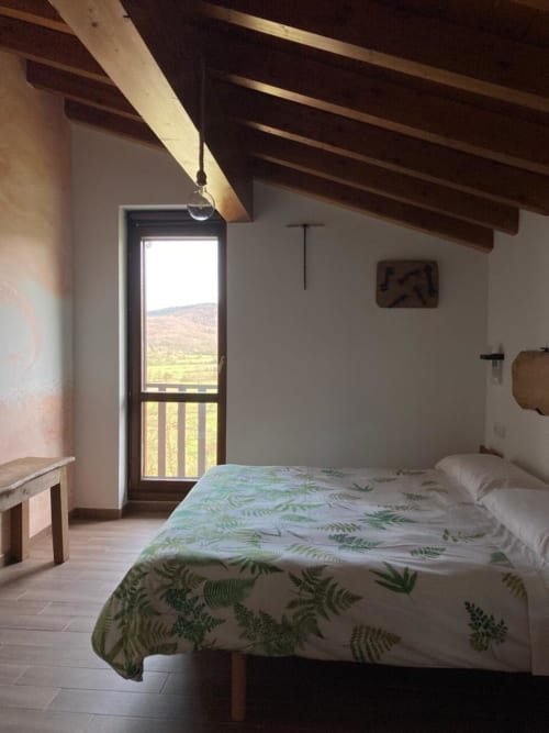 Habitación luminosa en Casa Lafuente con ropa de cama estampada de helechos, vigas de madera expuestas, balcón con vistas a la montaña, Lukiano
