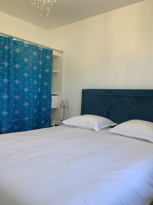 Bright bedroom at Locacharme cottage in Blois with blue patterned curtain, dark headboard, white pillows and bedding, crystal