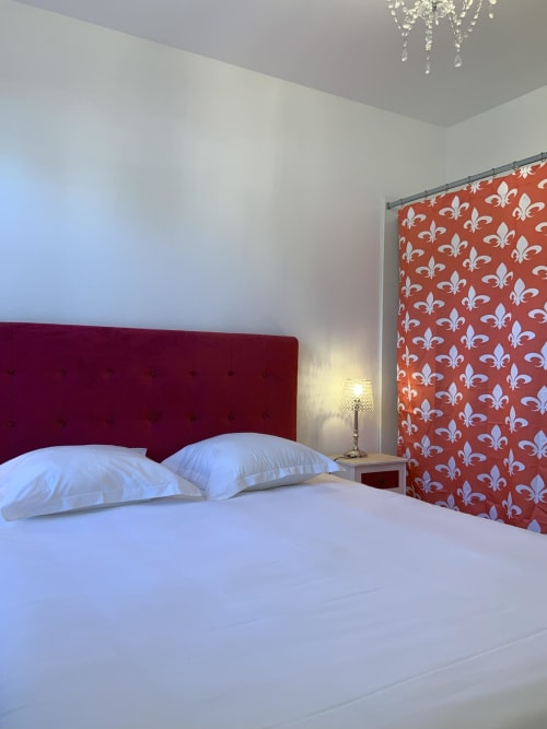 Modern bedroom with burgundy headboard, white linens, red fleur-de-lis wallpaper accent, and crystal chandelier at Locacharme