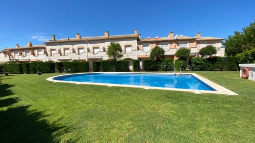 Cottage Mar Blau de Estartit con piscina ovalada azul, césped verde, edificios de terracota y cielo despejado