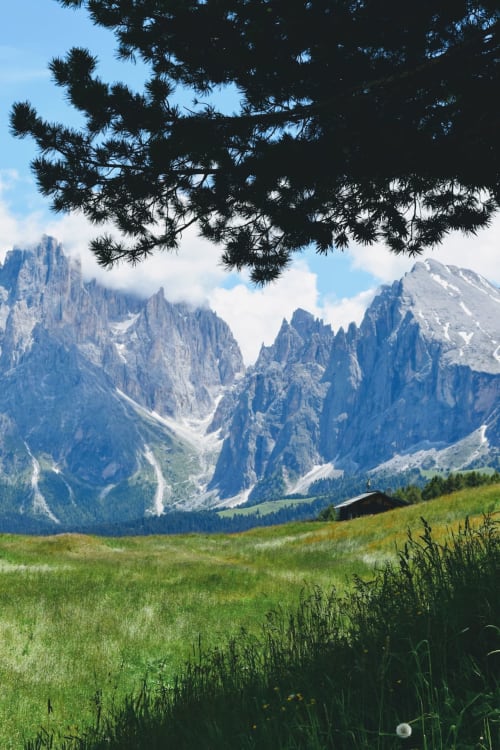 Valle alpina con picchi drammatici, prato verde e tradizionale chalet vicino a Treviso
