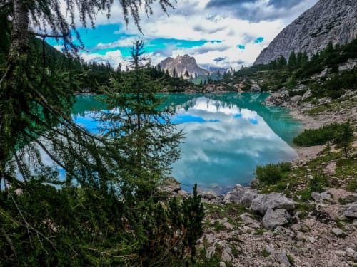 Lago alpino turchese circondato da montagne e foreste di conifere vicino a Treviso, Italia