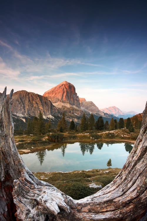 Lago alpino incorniciato da tronchi caduti, foresta di conifere e picchi drammatici vicino a Treviso