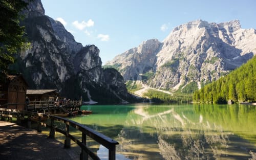 Lago alpino con acqua turchese cristallina, pontile in legno, montagne a strapiombo e fitti boschi vicino a Treviso