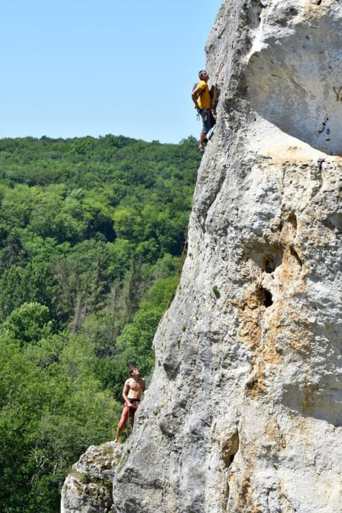 Escaladores ascendiendo un acantilado de piedra caliza con vistas al valle boscoso cerca del Domaine de l'Ocrerie en Pourrain, Francia