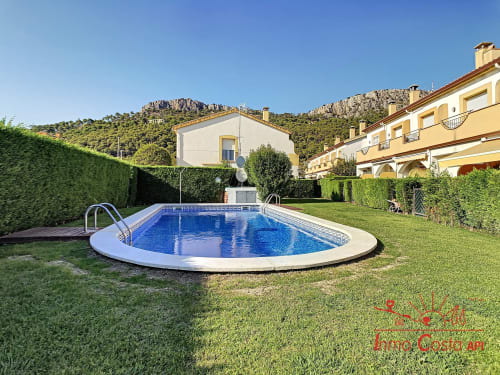 Piscina ovalada con borde blanco en exuberante jardín en Estartit Rental, L'Estartit, España, rodeada de villas amarillas y