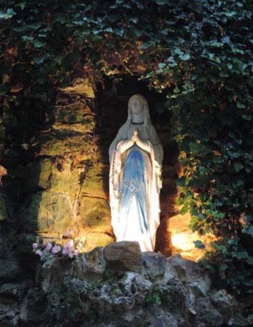 Beleuchtete Madonnenstatue in einer Grotte des Domaine de l'Ocrerie in Pourrain, umgeben von Efeu und violetten Blüten