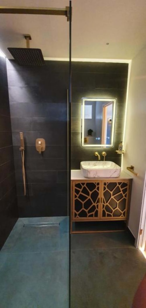 Modern bathroom in Dublin Exchange Suites with black tile shower, marble vessel sink, illuminated mirror, and wooden vanity