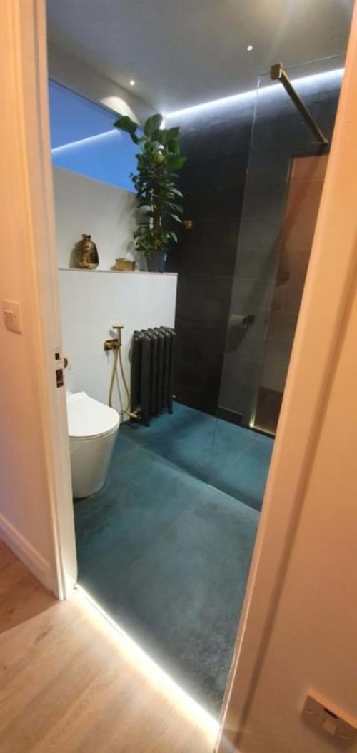 Modern bathroom in Dublin Exchange Suites with white toilet, black radiator, potted plant, and blue-tiled floor with ambient