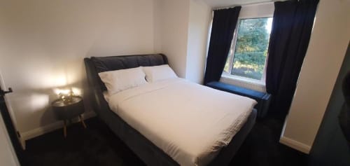Modern bedroom with black upholstered bed, white linens, bedside lamp, dark curtains, and garden view window at Dublin