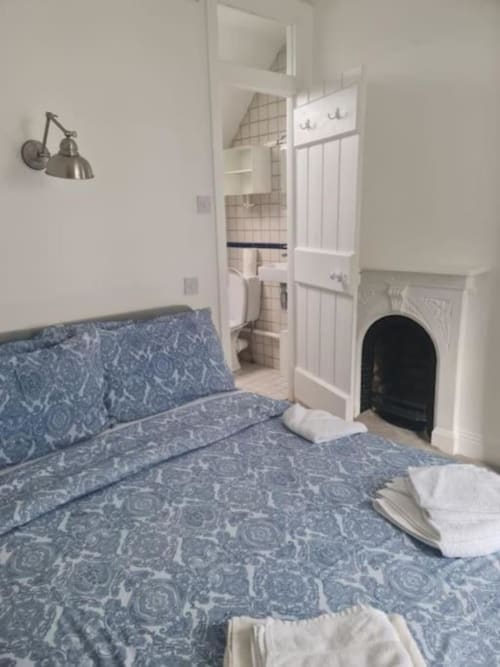 Cosy Irish cottage bedroom with blue patterned bedding, fireplace, ensuite bathroom, and wall-mounted lamp at Dublin Exchange