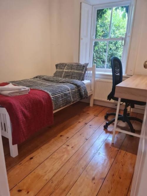 Bright bedroom in Dublin cottage with single bed, desk, black chair, wooden floors and garden view window