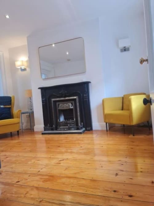 Bright sitting area with fireplace, yellow armchairs, hardwood floors, and mirror in Dublin cottage accommodation