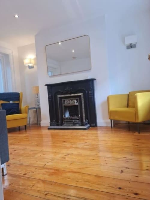Cosy Irish cottage living room with fireplace, yellow armchairs, wooden floors, and wall mirror at Dublin Exchange Suites