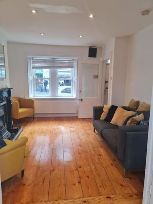 Modern living room with wooden floors, gray sofa with gold cushions, yellow armchair, fireplace, and large windows at Dublin