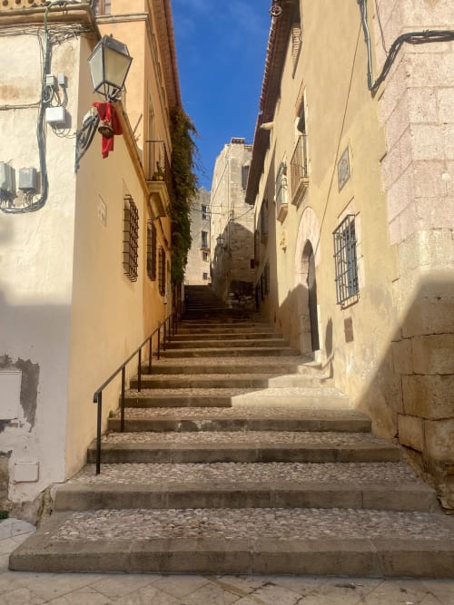 Estrecho tramo de escaleras adoquinadas en la histórica Altafulla con edificios de terracota y cielo azul despejado