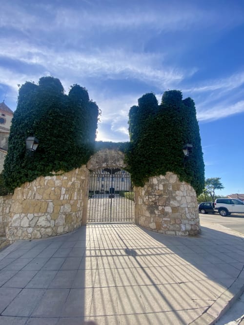 Entrada de portón de piedra cubierto de hiedra en el hotel BondBeach Village de Altafulla, España, con cielo azul