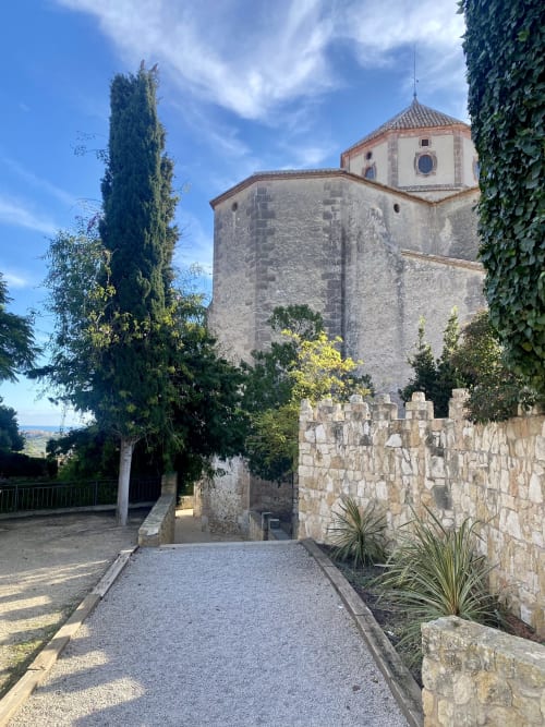 Iglesia histórica de piedra con cúpula de terracota en Altafulla, España, rodeada de cipreses y arquitectura mediterránea