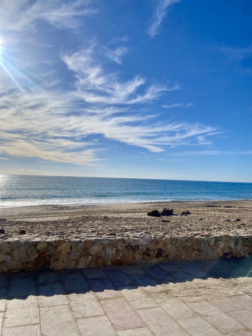 Playa de arena de BondBeach Village Altafulla con aguas turquesas, cielo azul y muro de piedra junto al mar