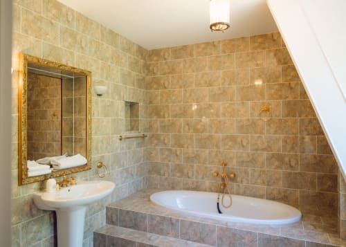 Salle de bain luxueuse avec carrelage en marbre, baignoire îlot, lavabo sur colonne et accessoires dorés au Domaine de Bize à Mirepoix