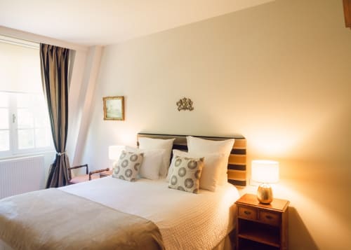 Dormitorio luminoso en Domaine de Bize con cabecero rayado, almohadas decorativas, iluminación cálida y vista al jardín