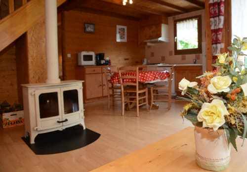 Intérieur cosy du gîte Des Planchettes avec poêle à bois, table à manger et roses jaunes au premier plan