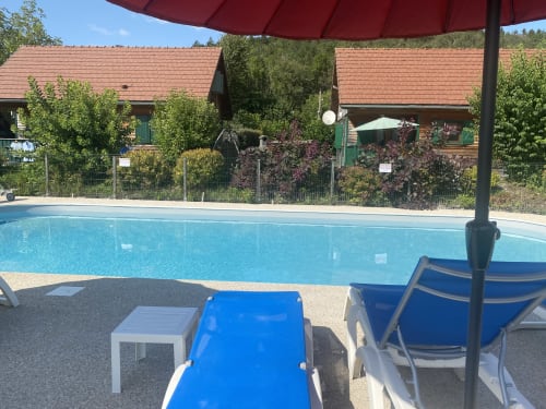 Piscine des Gîtes Des Planchettes à Marigny avec transats bleus, parasol rouge et bâtiments de gîtes