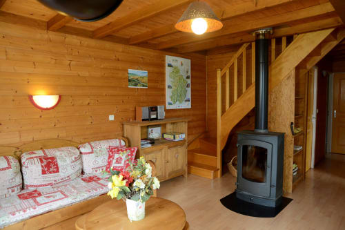 Intérieur cosy d'un chalet en bois aux Gîtes Des Planchettes avec poêle à bois, canapé motifs et mobilier rustique