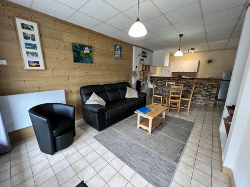 Séjour du gîte Des Planchettes avec canapé cuir noir, murs en bois et cuisine ouverte à Marigny, France