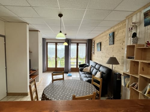 Séjour du gîte Des Planchettes à Marigny avec canapé noir, étagères en bois et accès à la terrasse