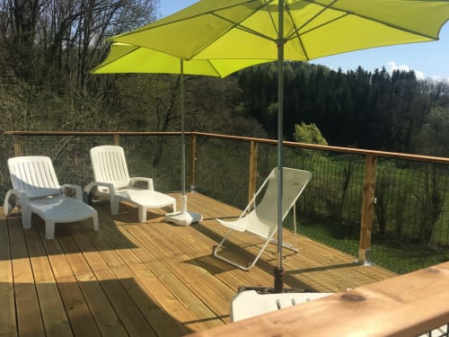 Terrasse ensoleillée des Gîtes Des Planchettes avec transats, parasol jaune et vue sur la forêt
