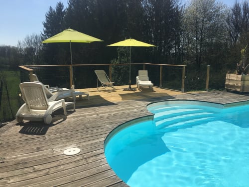 Terrasse ensoleillée de la piscine aux Gîtes Des Planchettes avec piscine bleue, transats, parasols jaunes et vue sur la forêt à Marigny