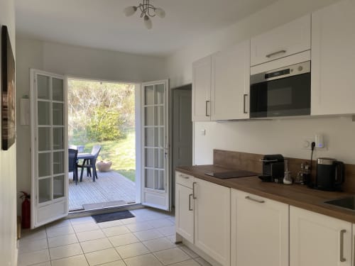 Modern kitchen with cream cabinets, wood countertops, and French doors opening to garden terrace at Domaine de Bize Mirepoix.