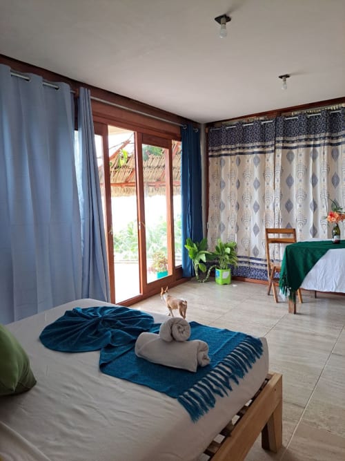 Amplia habitación en el hostal Cayuco Maya de Bacalar con vista al lago, cama de madera, detalles en azul y puertas de cristal al agua