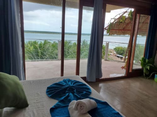 Vista del lago Bacalar desde una habitación del hostel Cayuco Maya con puertas de terraza abiertas y palmeras