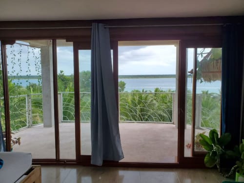 Habitación junto al lago en el hostel Cayuco Maya de Bacalar con puertas de vidrio abiertas hacia aguas tranquilas