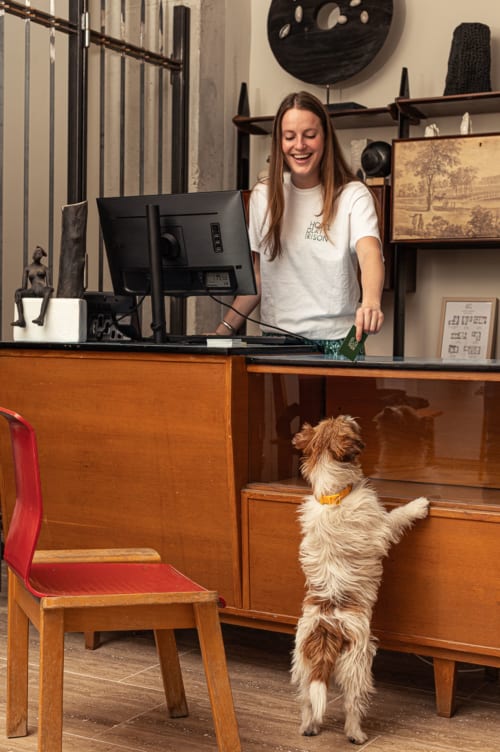 Mujer en la recepción del Hotel La Prison en Béziers con un perro pequeño de pie sobre sus patas traseras llevando un collar amarillo