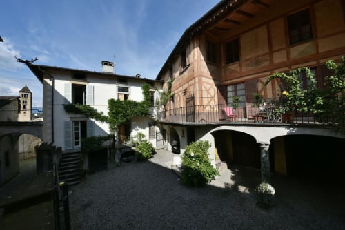 Cortile di Roseto del Drago a Ponte in Valtellina con edifici storici in pietra, muri ricoperti di edera e passaggio ad arco