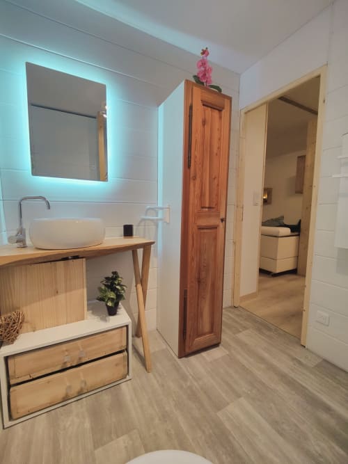 Salle de bain moderne à Location MarjoRI avec vasque, miroir rétroéclairé, meuble de salle de bain en bois et accès à la chambre